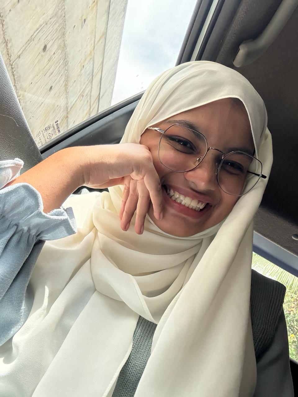 Aami smiling in a cream hijab and glasses